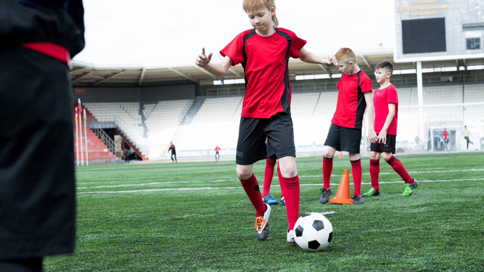 Full length portrait of junior football team practicing in stadium focus on boy leading ball in foreground, copy space
